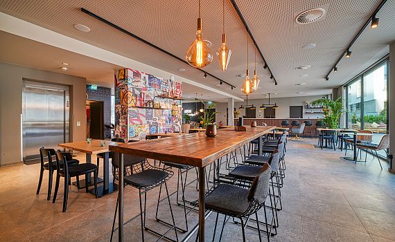 long table, many chairs, lamps, plant, colorful wall, rezeption in the background